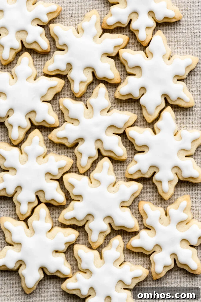 Overhead of snowflake shaped cookies with white icing on a cloth.