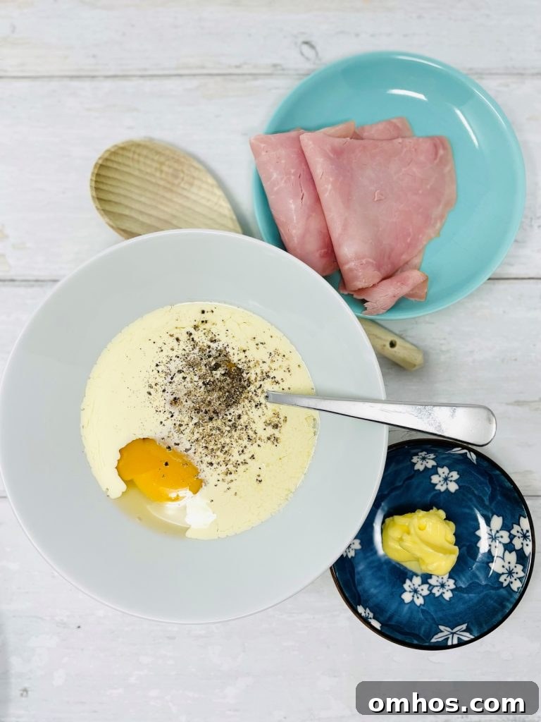 Slices of ham and butter beside a bowl of whisked egg and milk with pepper