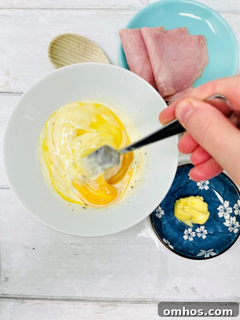 Whisked egg and milk in a bowl, ham and butter ready to cook