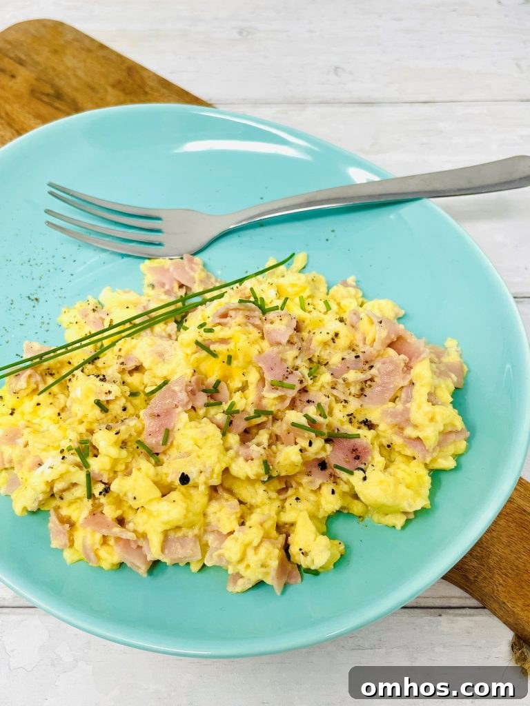 Scrambled eggs with ham on a blue plate next to a fork