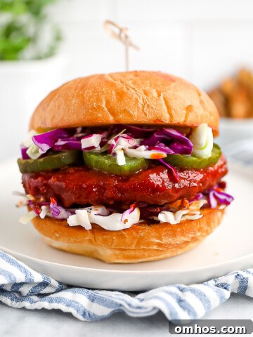 A sandwich with a sauce covered vegan patty, pickles, and coleslaw between two buns.