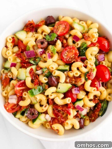 A veggie-filled pasta salad in a white bowl.