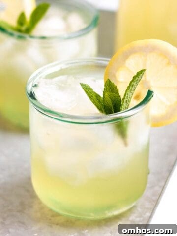 A glass of lemonade with a fresh lemon and mint.