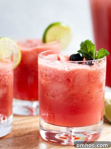Three old fashioned glasses with watermelon limeade, slices of fresh lemons, mint leaves and blueberries.