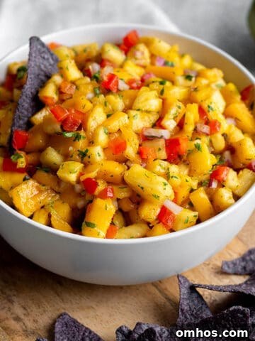 A bowl with diced mangos, pineapples and blue corn tortilla chips on a wooden board.
