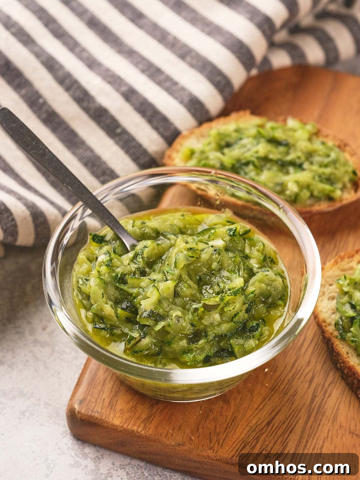 A small glass bowl of grated zucchini with butter and herbs, placed on a wooden board.