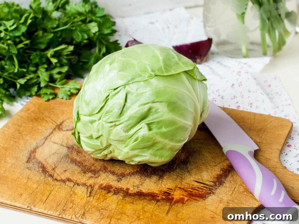 A fresh green cabbage on a wooden cutting board with a purple knife beside it, set against a backdrop of parsley and onions.