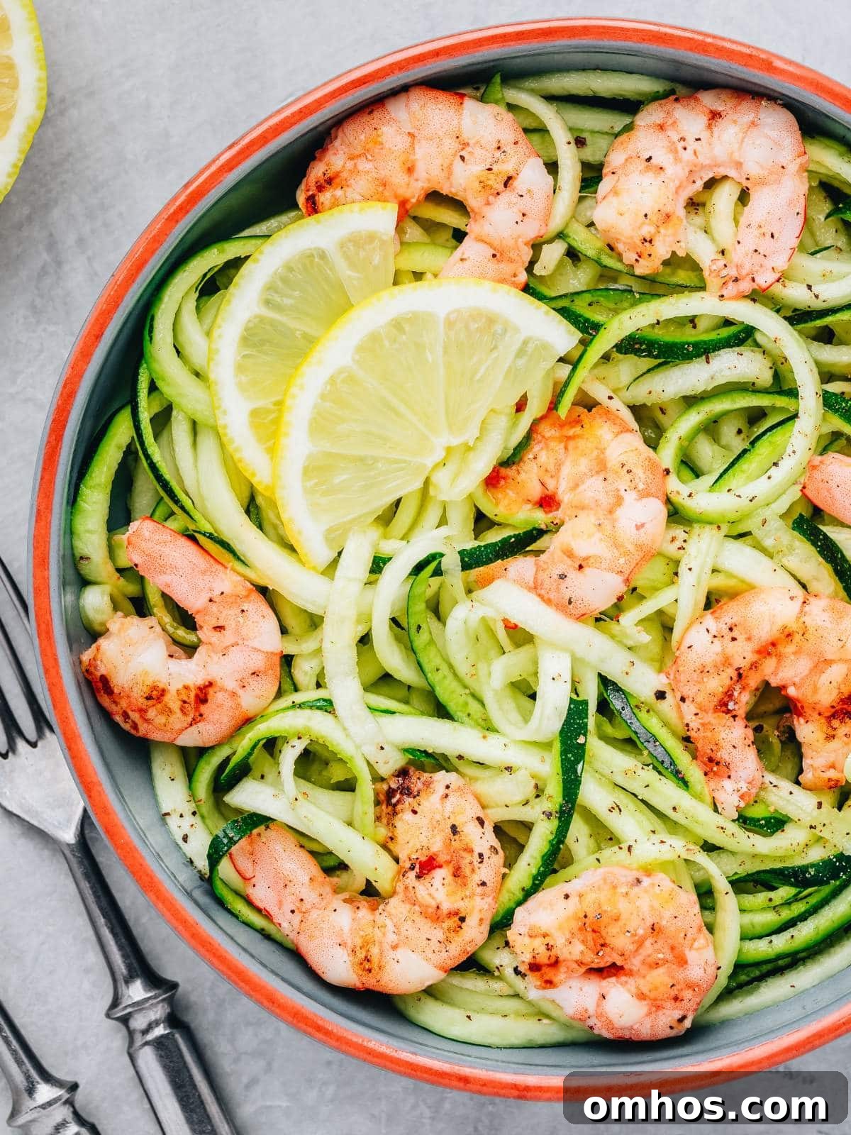 A bowl of zucchini noodles topped with grilled shrimp and lemon slices.