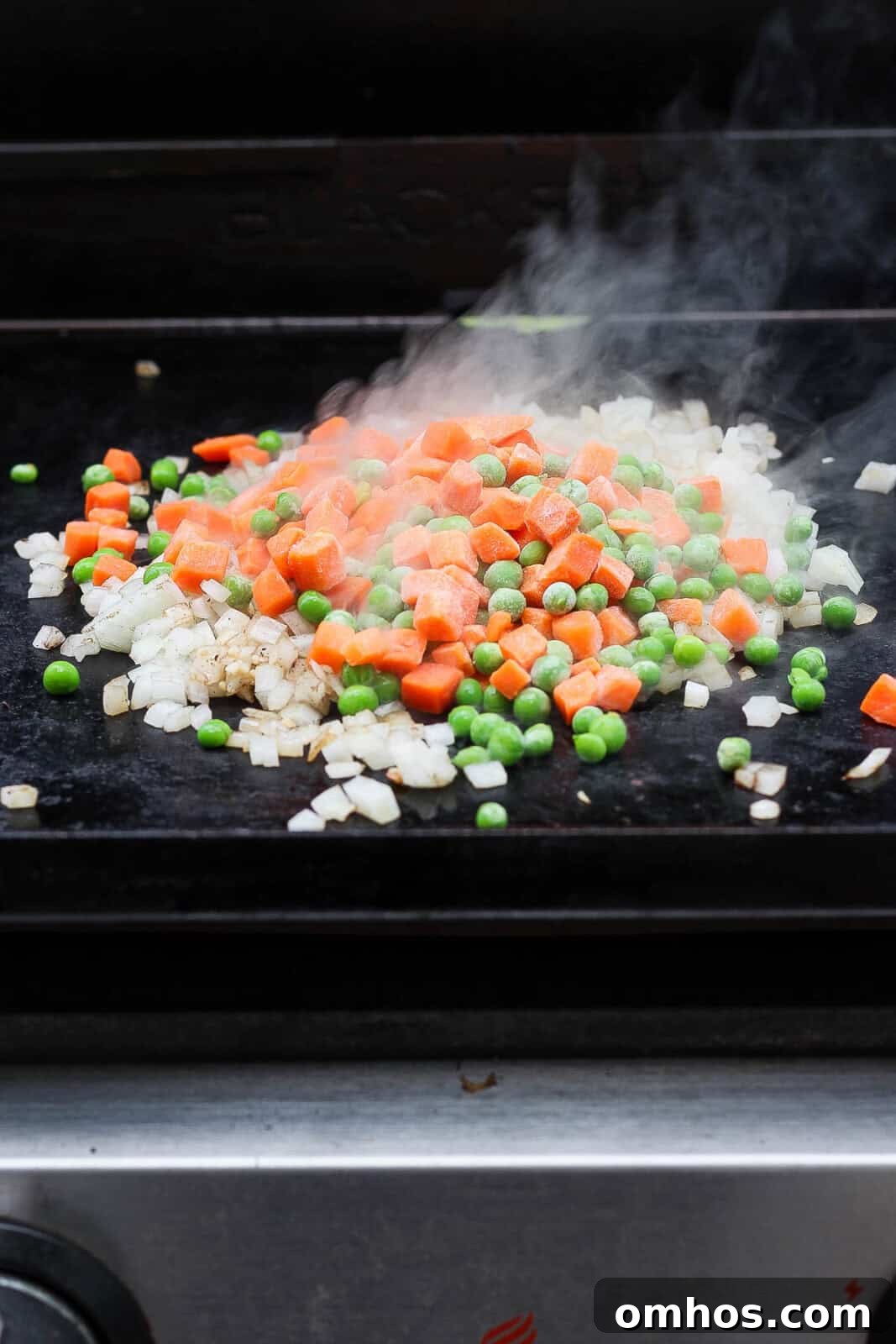 Sautéed onion and garlic with frozen peas and carrots for Blackstone shrimp fried rice.