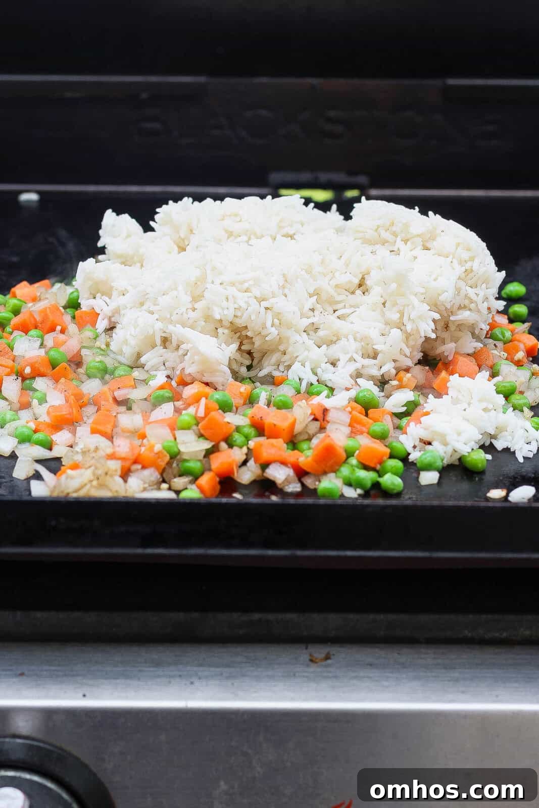 Rice added to the veggies on the griddle for Blackstone shrimp fried rice.