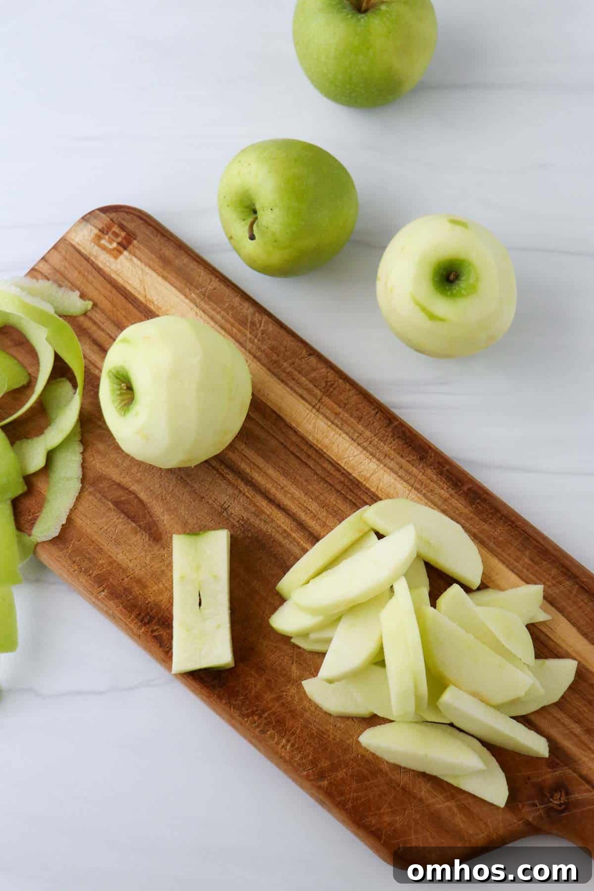 Sliced apples and a peeled apple on a wooden cutting board.