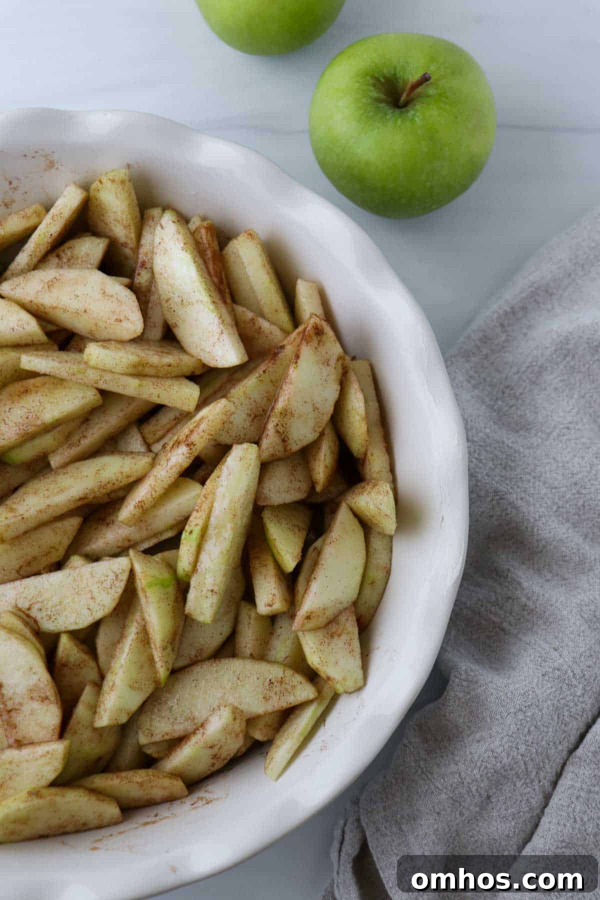 Apples tossed with spices in a pie plate.