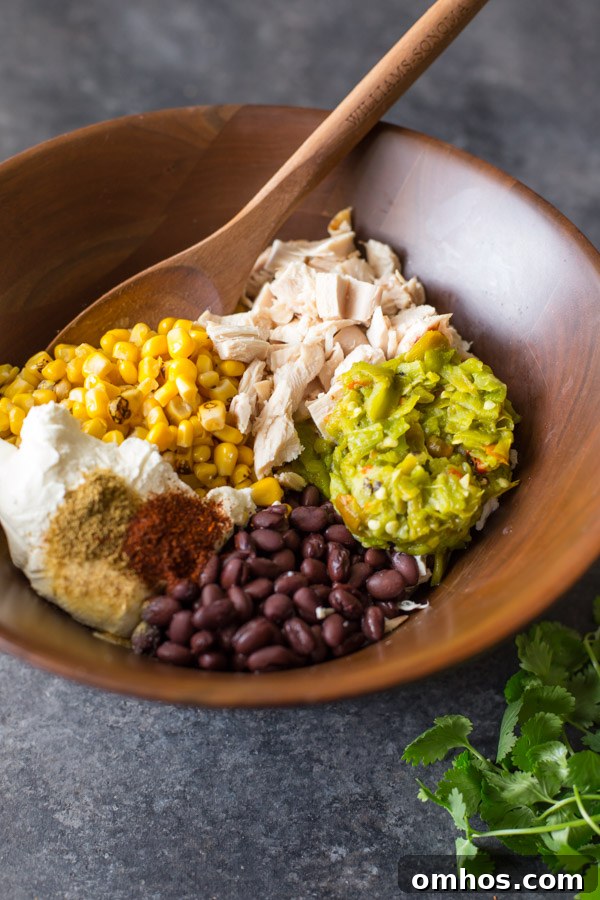 All the ingredients for the filling of the Hatch Green Chile Chicken Enchiladas in a large wood bowl with a wooden spoon in it. 
