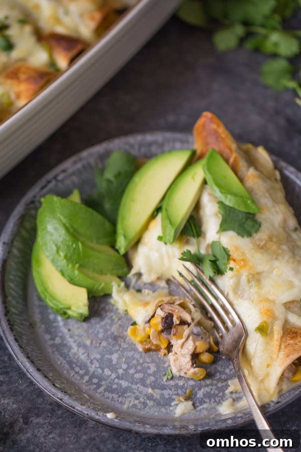 Hatch Green Chile Chicken Enchiladas on a plate with avocado slices, cilantro and a fork, sitting next to the baking dish of enchiladas.  