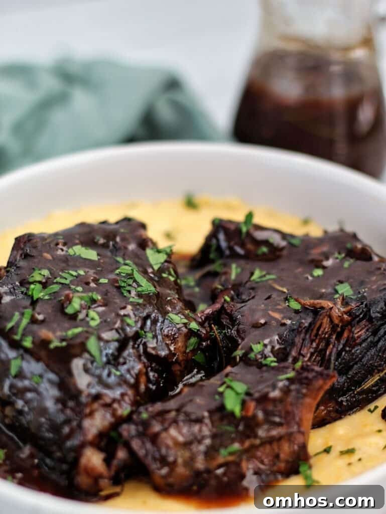 red wine braised pot roast on top of cheesy grits in a white shallow bowl.