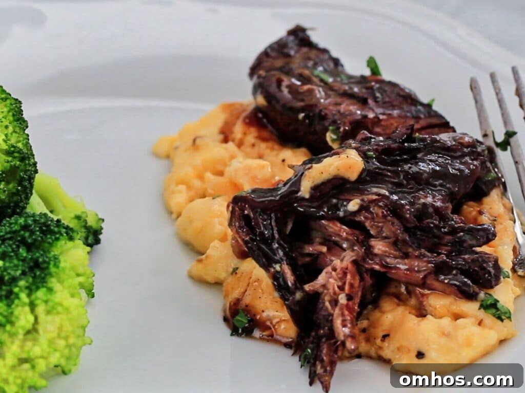 white plate with pot roast served atop cheese grits with a side of broccoli.