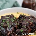 red wine braised pot roast on top of cheesy grits in a white shallow bowl.