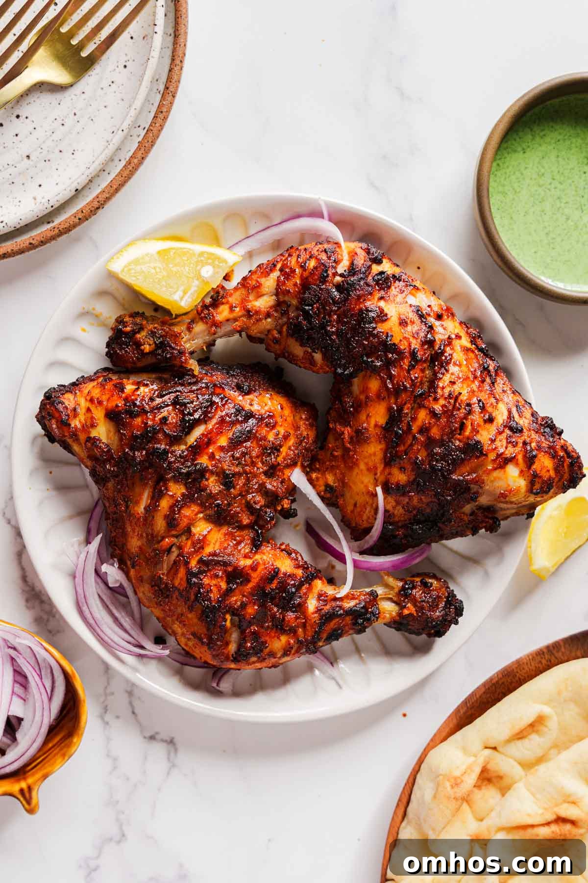 air fryer tandoori chicken on a plate with onion and green chutney on the side.
