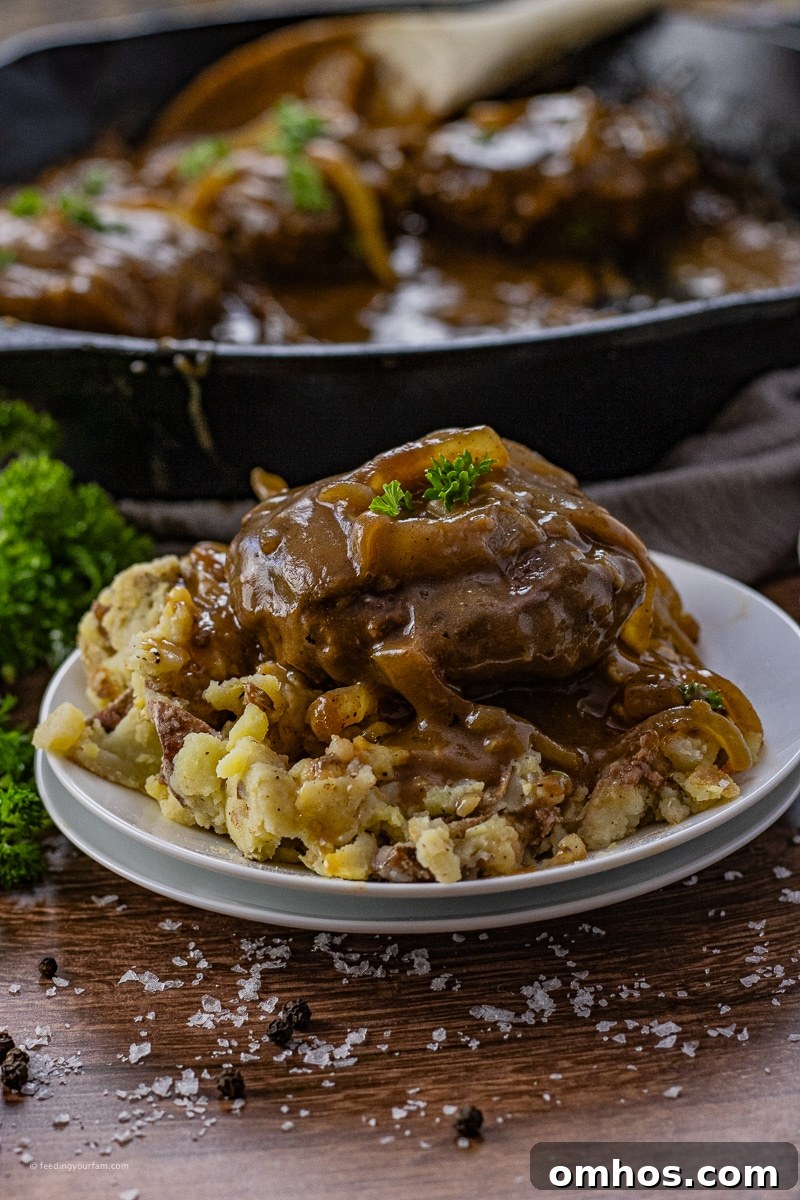 onion gravy hamburger steaks over mashed potatoes on a round, white plate