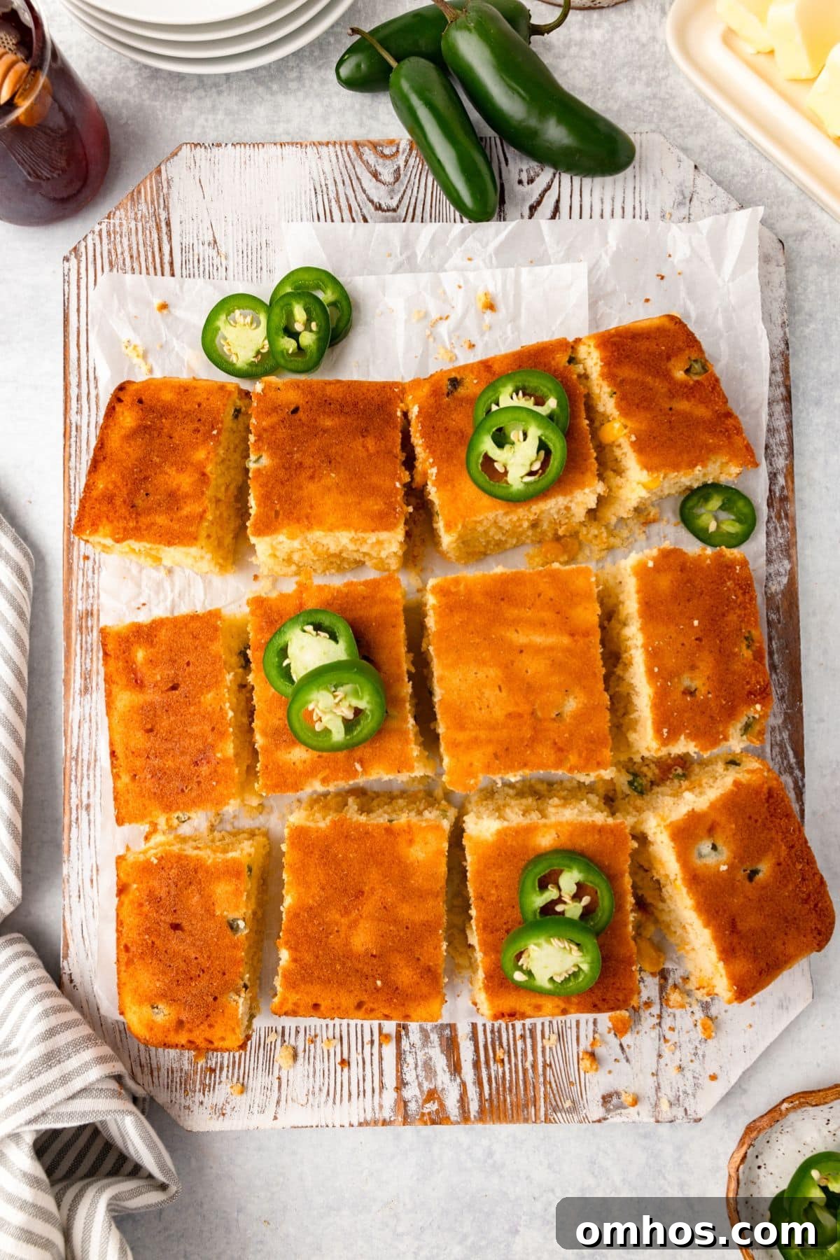 Skillet Jalapeño Cornbread Recipe 6 Sliced cornbread topped with jalapeño slices on a wooden board lined with parchment paper.