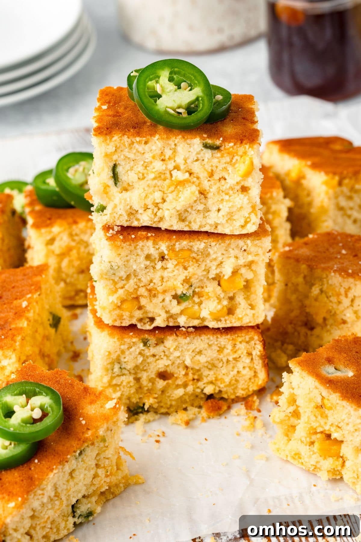 Skillet Jalapeño Cornbread Recipe 8 A stack of three pieces of cornbread garnished with sliced jalapeños on top.