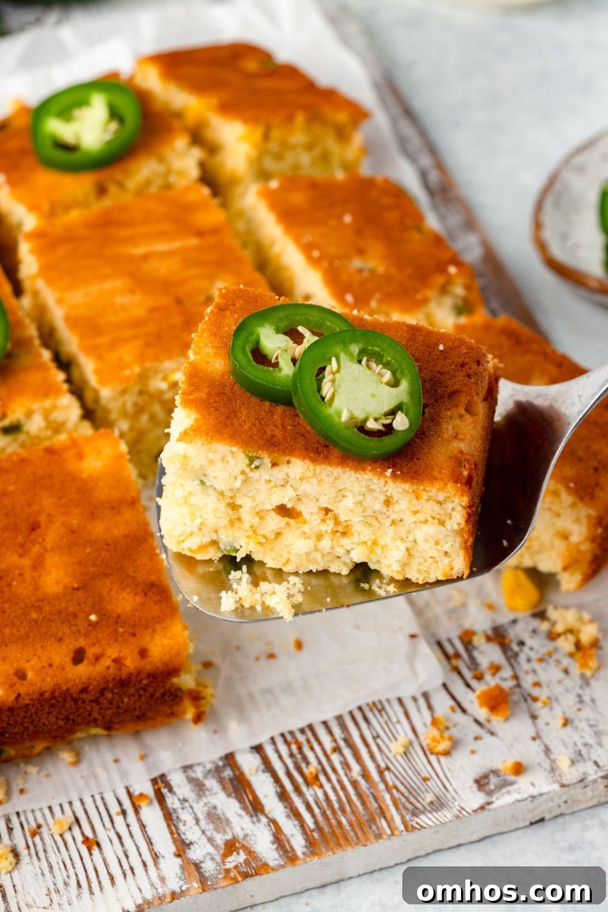Skillet Jalapeño Cornbread Recipe 9 A piece of cornbread topped with sliced jalapeños is held up on a spatula.