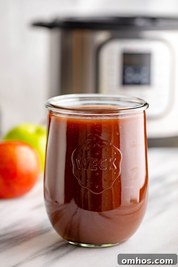 No-Peel Instant Pot Apple Butter Recipe 2 weck jar filled with apple butter with a red and green apple in the background along with an instapot