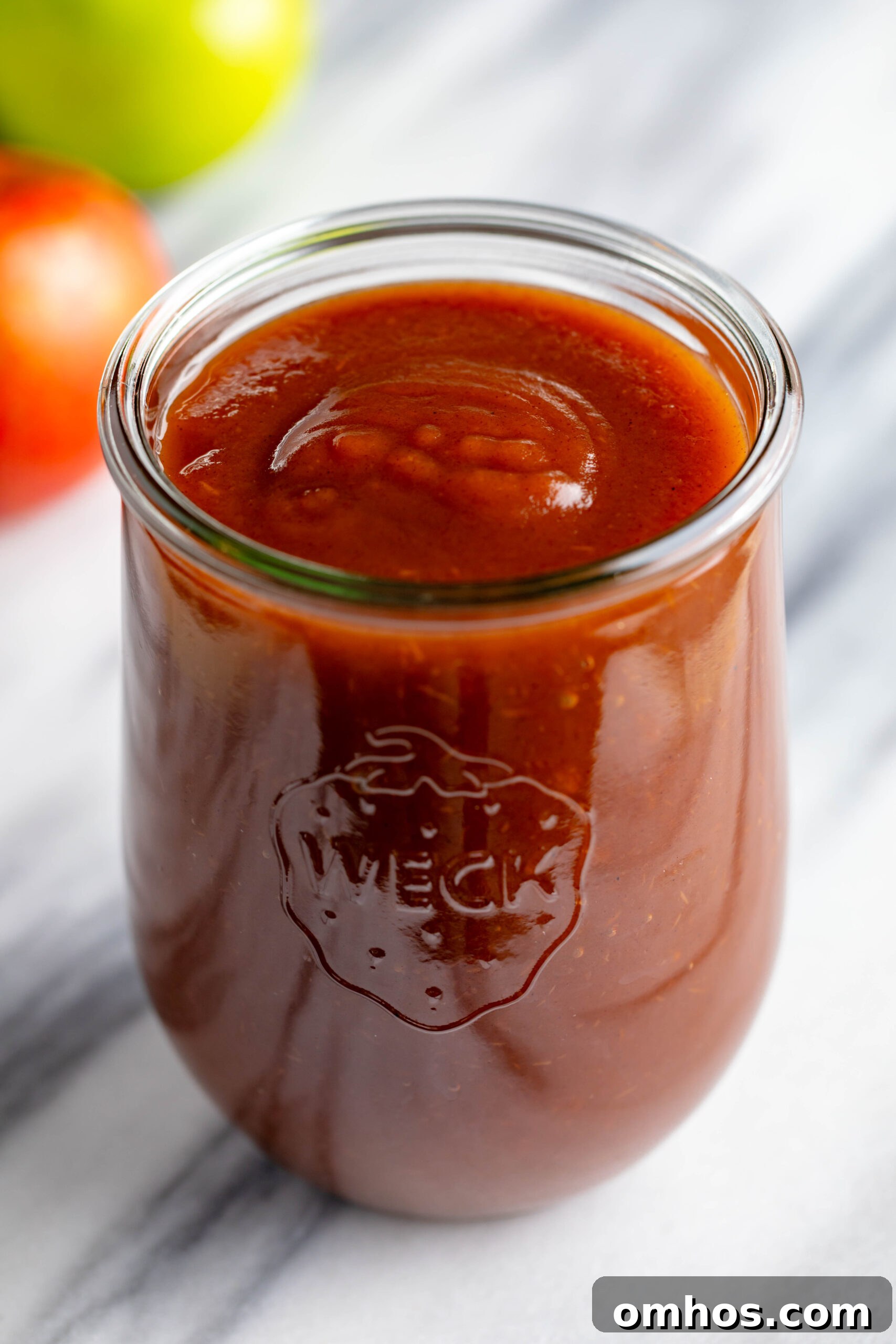 No-Peel Instant Pot Apple Butter Recipe 12 weck jar filled with apple butter on a white marble slab with a red and green apple in the background