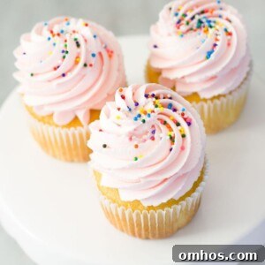 Homemade Cotton Candy Frosting Recipe for Cakes and Cupcakes 3 Three cupcakes with pink frosting and sprinkles on a cake stand