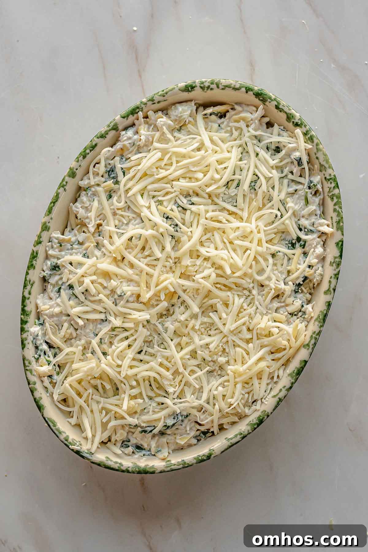 Shredded cheese sits on top of crab spinach dip prior to baking.