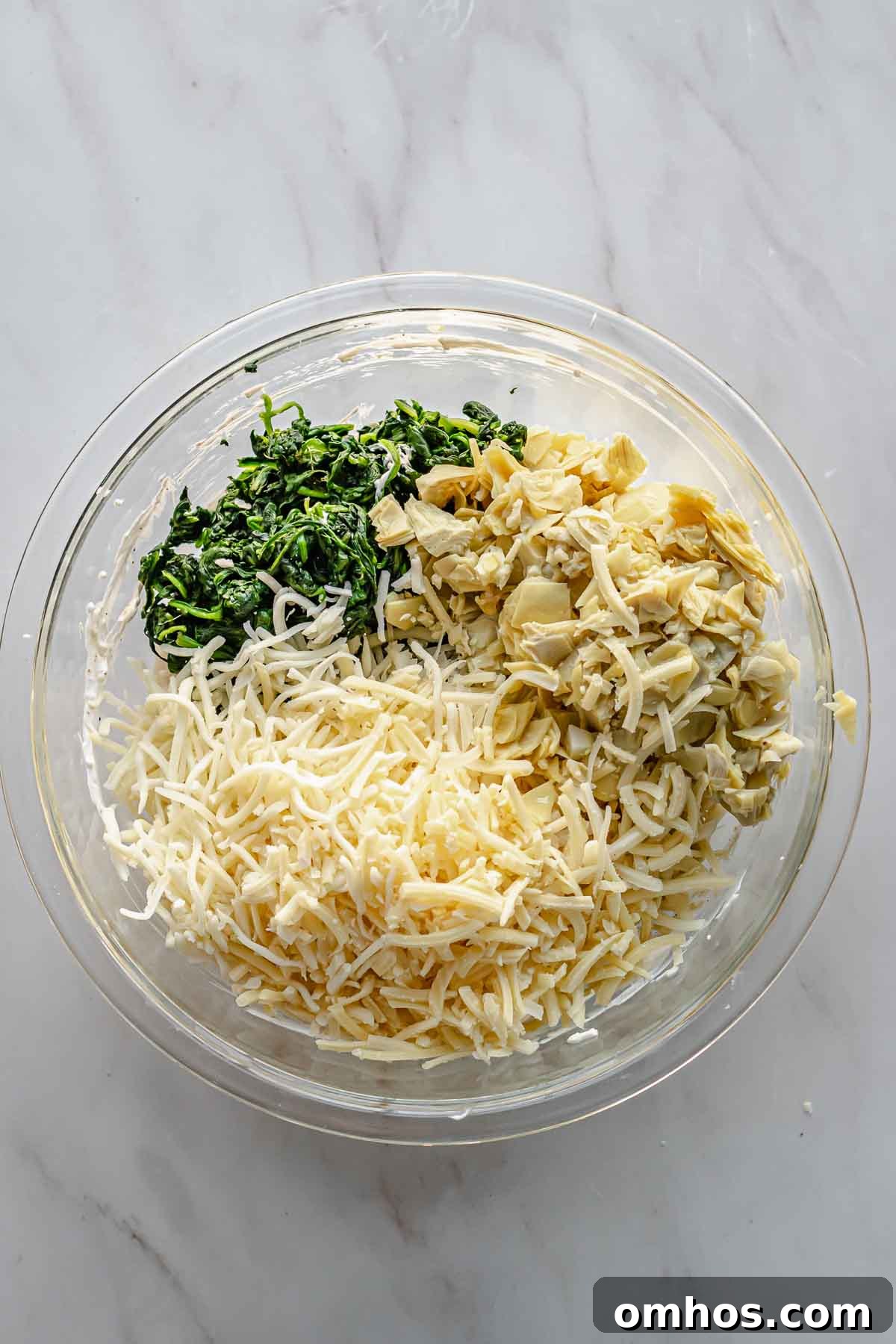 Cheeses, chopped artichokes, and chopped spinach in a bowl.