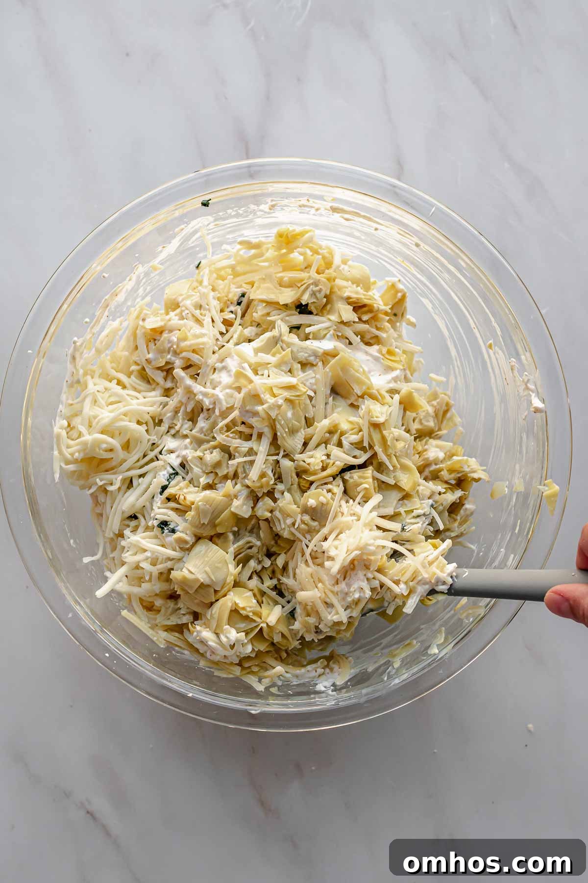 A spatula mixes spinach artichoke dip in a bowl.