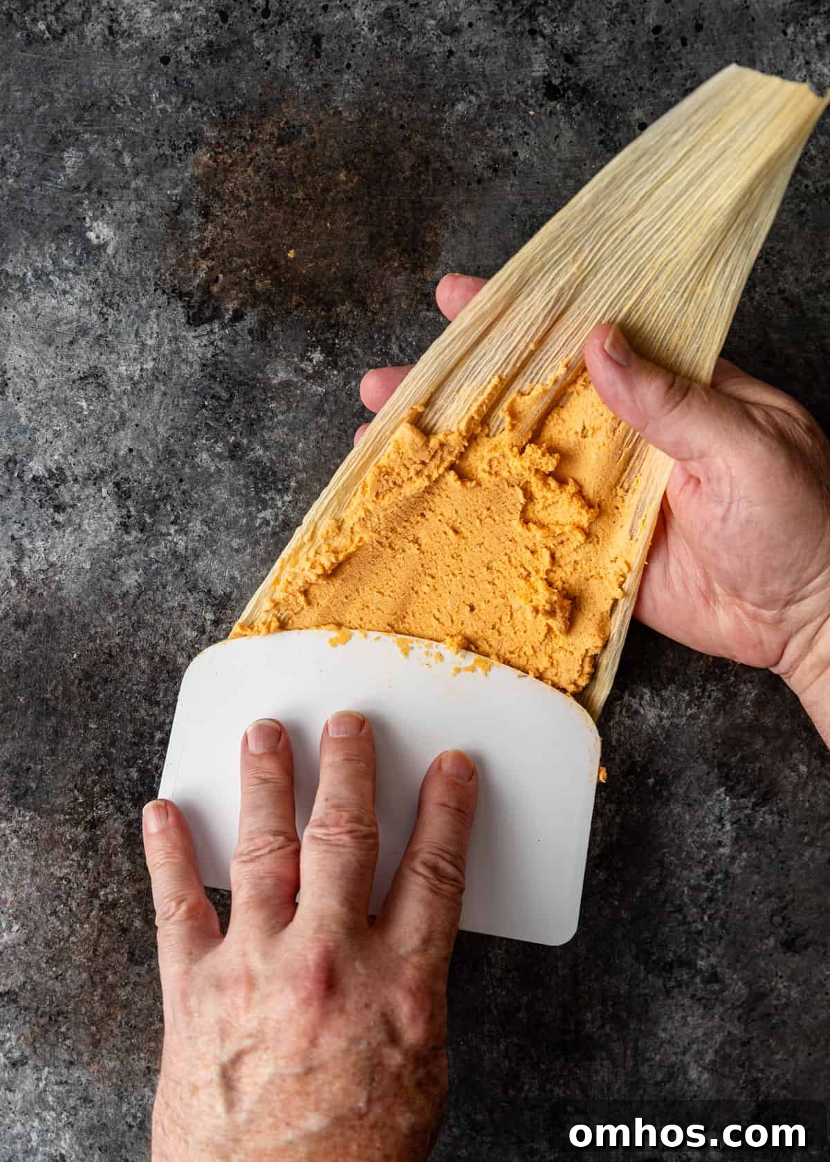 Authentic Mexican Red Pork Tamales Recipe 7 overhead process shot: titled image (and shown) adding masa