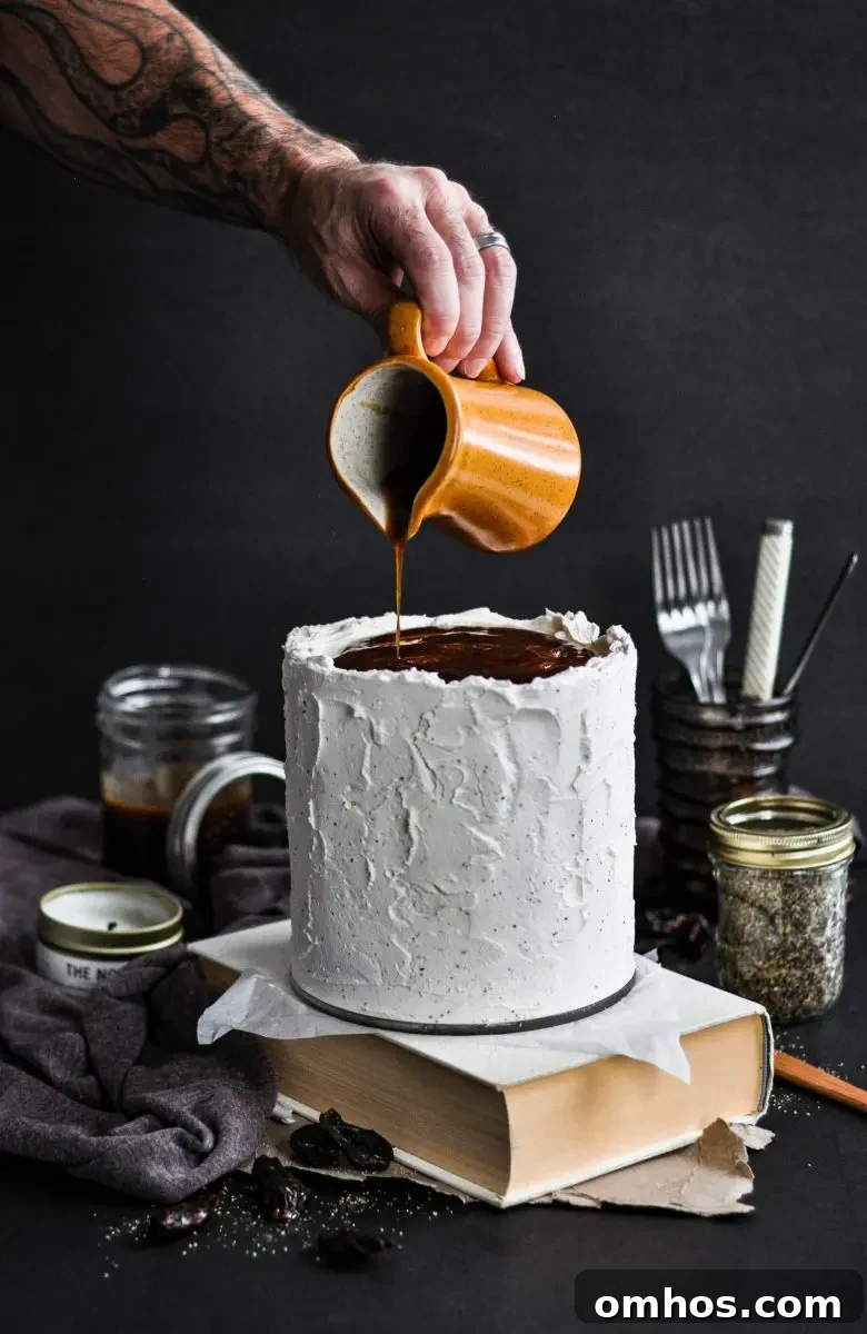 A white frosted sticky toffee pudding cake. There is someone pouring toffee sauce over the top of the cake.