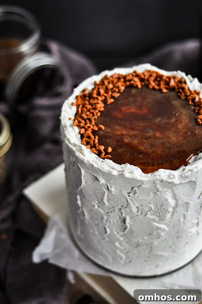 A white frosted cake with black pepper speckles in the frosting. It is topped with toffee sauce and toffee bits.
