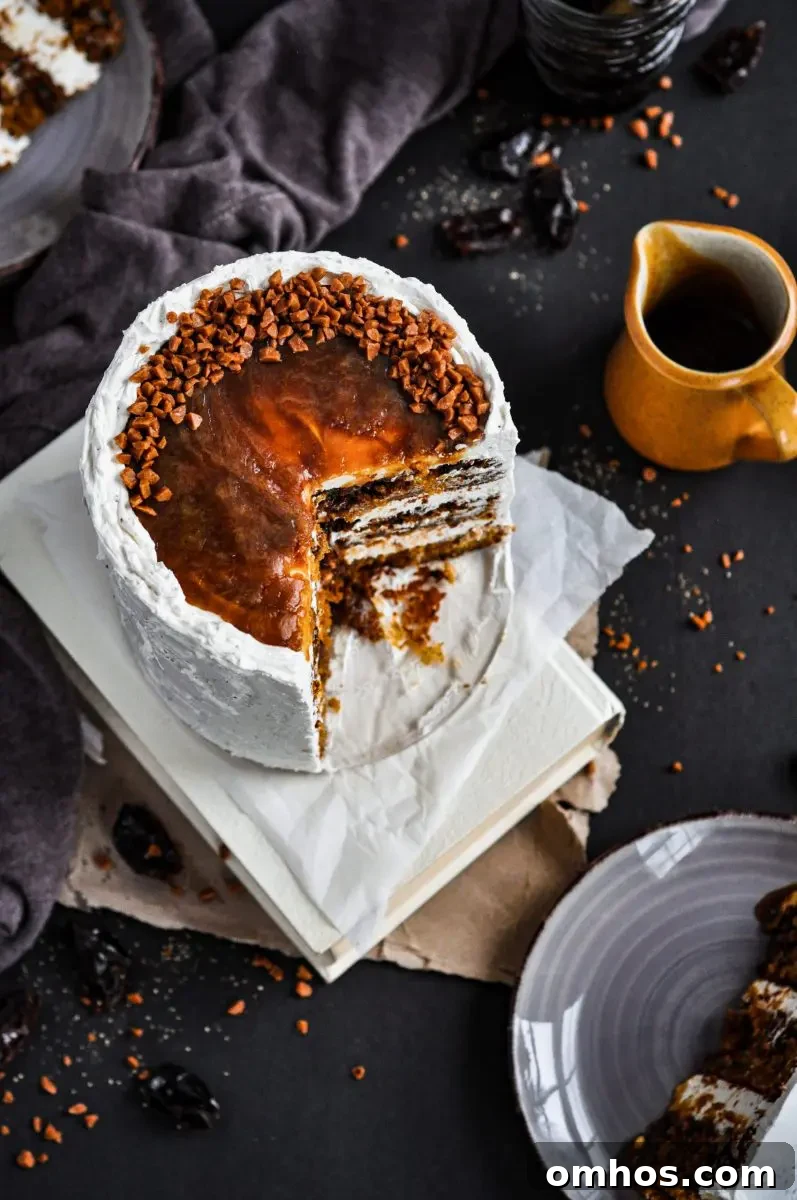 A white frosted cake with black pepper speckles in the frosting. It is topped with toffee sauce and toffee bits. There is a large slice taken out of the cake.