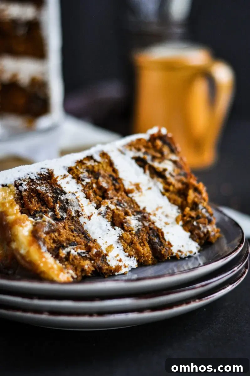 A slice of sticky toffee pudding layer cake sitting on a plate. It has white frosting between each cake layer.