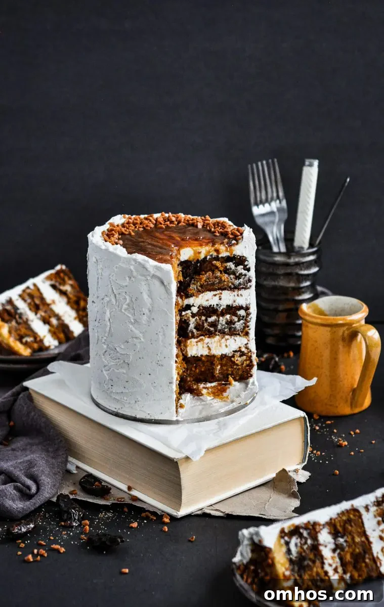 A sticky toffee pudding cake covered in white frosting topped with toffee sauce. There are two slice taken out of the cake showing you the inside cake layers.