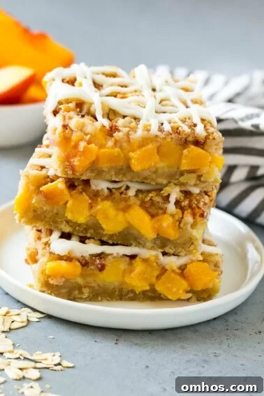 A stack of peach crumble bars topped with vanilla glaze.